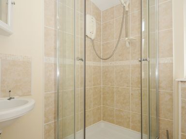 A bathroom shower enclosure with beige tiles a white electric shower and a partial view of a white sink at Little Trebah Atlantic Bays Holiday Park near St Merryn