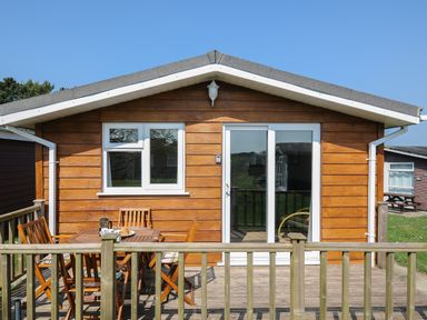 A wooden cabin with a small patio with table and chairs at Little Trebah Atlantic Bays Holiday Park near St Merryn