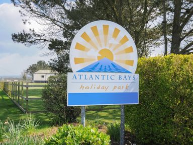 A sign for Atlantic Bays holiday park with trees fence and grass at Atlantic Bays Holiday Park near St Merryn