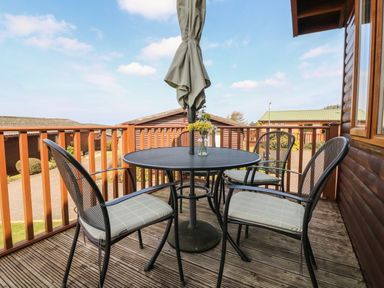 A balcony with a round table and four chairs with cushions and an umbrella at Seascape Retreat in Ilfracombe