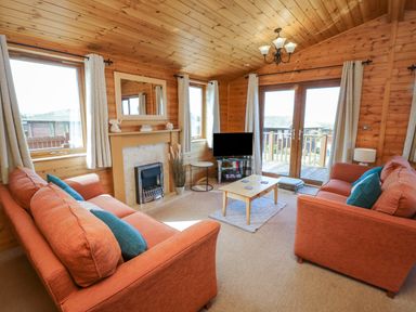 A living room with two orange sofas a wooden coffee table a fireplace a TV and windows with curtains at Seascape Retreat in Ilfracombe