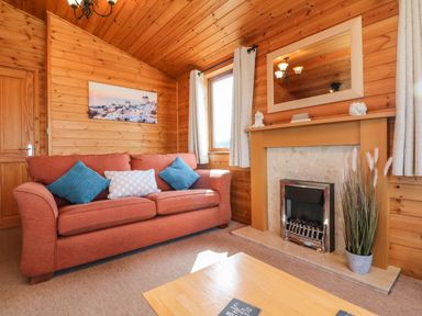 A living room with a red sofa and blue cushions next to a fireplace and a window at Seascape Retreat in Ilfracombe