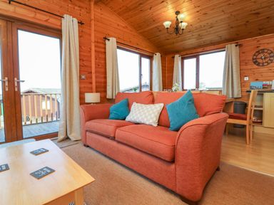 A living room with a red sofa and blue pillows next to wooden windows and a wooden coffee table at Seascape Retreat in Ilfracombe