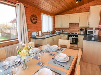 A dining table set with plates bowls and glasses next to a kitchen area with cabinets an oven and a microwave at Seascape Retreat in Ilfracombe