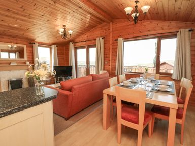 A dining table set with dishes and glasses next to a living room with a red sofa and a television in a wood-paneled room at Seascape Retreat in Ilfracombe