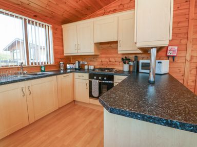 A kitchen with light wood cabinets black countertops a sink toaster kettle microwave and utensils at Seascape Retreat in Ilfracombe