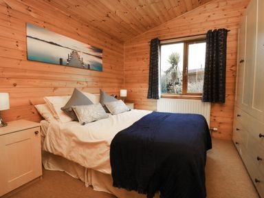 A bedroom with wooden walls a bed with pillows bedside tables lamps and a window with curtains at Seascape Retreat Ilfracombe