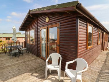 An outdoor deck with plastic chairs and a dining table next to a wooden cabin at Seascape Retreat in Ilfracombe