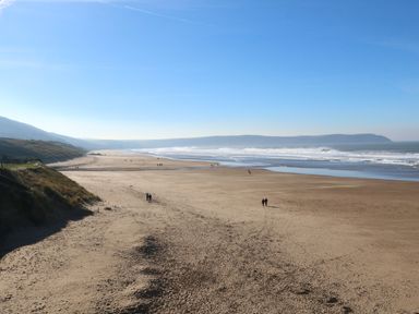 A wide sandy beach with people walking near the ocean and hills in the background at Seascape Retreat in Ilfracombe