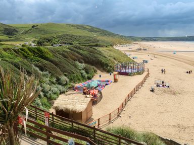A beach with a fenced play area and grassy hills in the background at Seascape Retreat in Ilfracombe