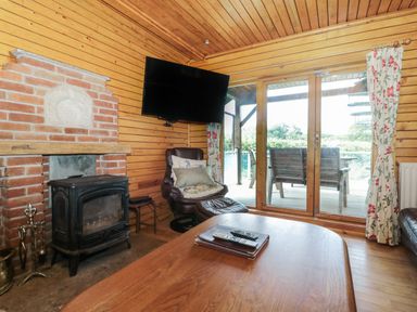 A wooden interior living room with a wood-burning stove a leather armchair a television and glass doors leading to an outdoor seating area at Ash in Swanage