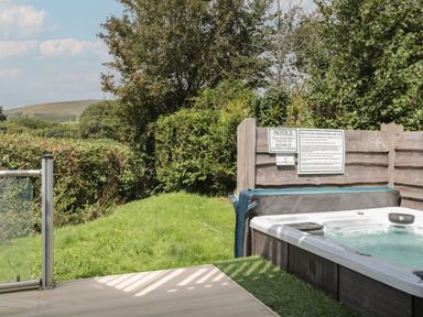 An outdoor hot tub with safety notice boards on a wooden fence surrounded by grass and trees at Ash in Swanage