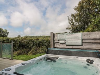 An outdoor hot tub with informational signs on a wooden fence and a hedge in the background at Ash in Swanage