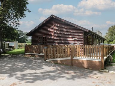 A wooden cabin with a fenced deck and trees around it at Ash in Swanage