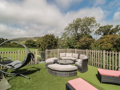 An outdoor seating area with cushioned wicker furniture and hanging chair on artificial grass next to a wooden fence at Ash in Swanage