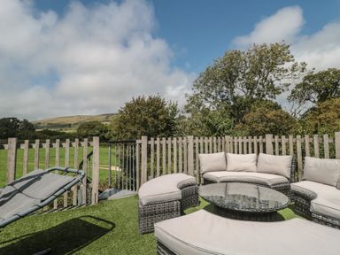 An outdoor seating area with cushioned wicker furniture and a glass-top table on artificial grass at Ash Swanage