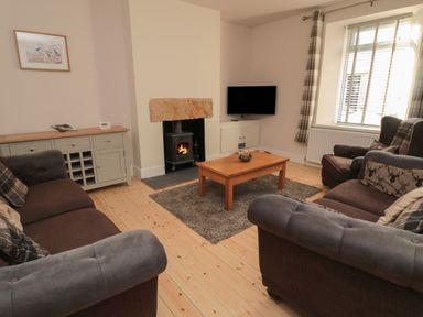 A living room with sofas a wooden coffee table a wood burner and a television at 55 Wellwood Street in Amble