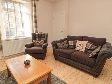 A living room with a brown sofa and armchair with patterned cushions next to a wooden coffee table at 55 Wellwood Street in Amble