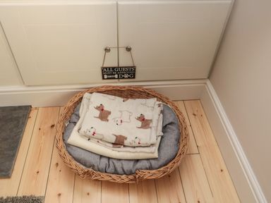 A dog bed with blankets on a wooden floor under a cabinet with a sign at 55 Wellwood Street in Amble