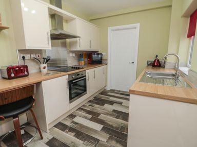 A kitchen with white cabinets wooden countertops stainless steel sink and stove a red toaster and kettle on the counter at 55 Wellwood Street in Amble