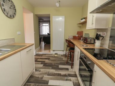 A kitchen with a wooden countertop and white cabinets two chairs by the counter a wall clock and a large vertical radiator at 55 Wellwood Street in Amble