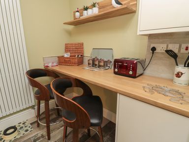 A kitchen counter with two wooden stools a red toaster kitchen utensils and a wicker basket at 55 Wellwood Street in Amble