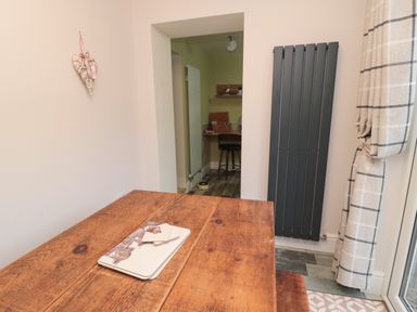 A wooden dining table with placemats in a room with a black vertical radiator and checked curtains at 55 Wellwood Street in Amble