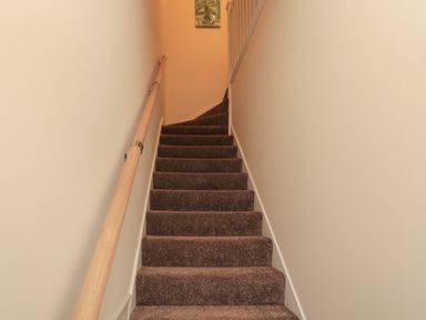 A carpeted staircase with a wooden handrail and a picture on the wall at 55 Wellwood Street in Amble
