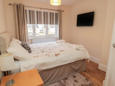 A bedroom with a bed a bedside table with a lamp a window with curtains and a mounted television at 55 Wellwood Street in Amble