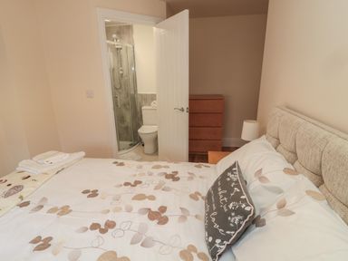 A bedroom with a bed a bedside table with a lamp a chest of drawers and an ensuite bathroom at 55 Wellwood Street in Amble