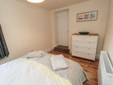 A bedroom with a bed with folded towels a white chest of drawers a door and a radiator at 55 Wellwood Street in Amble