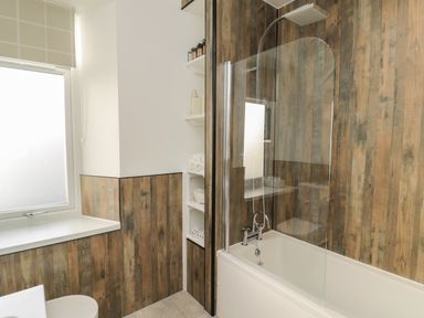 A bathroom with a bathtub and shower with wood panel walls and a window at 55 Wellwood Street Amble