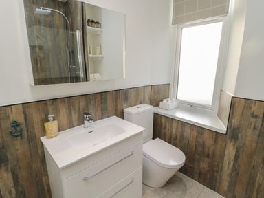 A bathroom with a white sink cabinet a toilet a window and wood paneling at 55 Wellwood Street in Amble