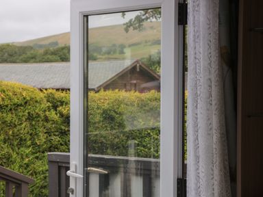 An open glass door with white frame showing a hedge and rooftops outside with hills in the background at Beech in Swanage