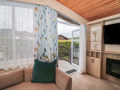 A living room with a beige sofa a green cushion curtains and a glass door leading to a wooden deck at Beech in Swanage