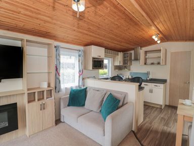 A living area with a sofa and cushions next to a kitchen with cabinets and appliances at Beech in Swanage