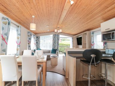 An open plan living and dining area with white chairs wooden table a sofa and bar stools at Beech in Swanage