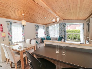 A living area with a dining table and chairs a corner sofa and bar stools at Beech in Swanage