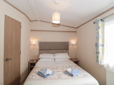 A bedroom with a double bed two bedside tables a wooden door and a window with patterned curtains at Beech in Swanage