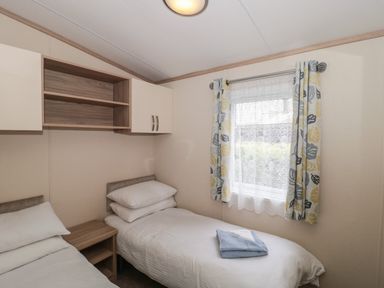A bedroom with two single beds a window with curtains and a small wooden bedside table at Beech in Swanage