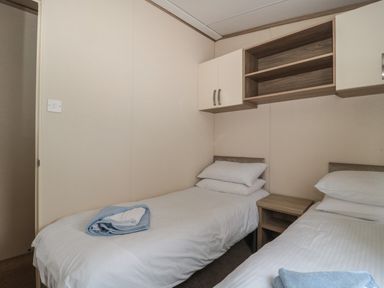 A bedroom with two single beds a small wooden nightstand and wall cabinets at Beech in Swanage