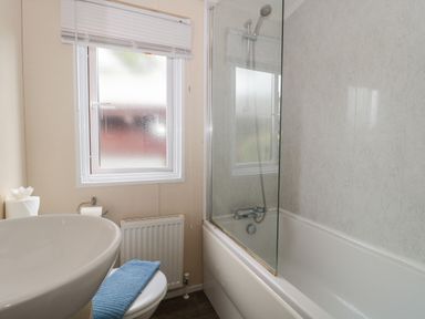A bathroom with a bathtub with shower head a sink a toilet with blue towel and a frosted window at Beech in Swanage