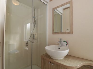 A bathroom with a shower enclosure a round sink with a faucet a mirror and a wooden countertop at Beech in Swanage