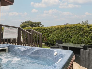 An outdoor hot tub with bubbling water next to a glass table and four wicker chairs behind a wooden railing and hedge at Beech in Swanage