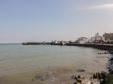 A coastal scene with a pier extending into the sea and buildings along a promenade at Beech in Swanage