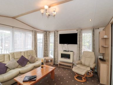 A living room with a leather sofa and armchair a wooden coffee table a wall-mounted TV and a fireplace at Birch in Swanage