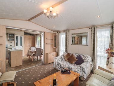 A living room with sofas a wooden coffee table and a kitchen and dining area visible through an open doorway at Birch in Swanage