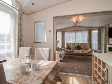 A dining area with a table covered by a map print tablecloth and two white mugs next to a living room with sofas and a coffee table at Birch Swanage