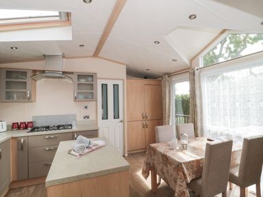 A kitchen with a gas stove chimney and cabinets next to a dining table with four chairs and large windows at Birch in Swanage