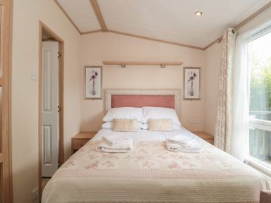A bedroom with a bed with pillows and folded towels two framed floral pictures and a window with curtains at Birch in Swanage